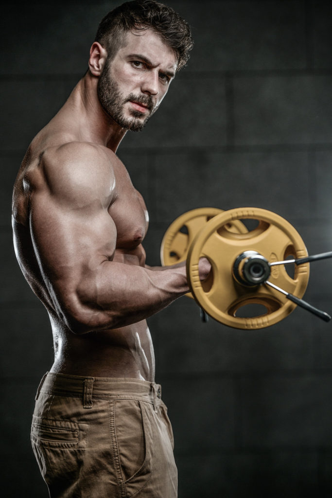 Handsome muscular Caucasian man of model appearance working out training arms in gym gaining weight pumping up muscles bicep and tricep with dumbbells and on machines fitness and bodybuilding concept