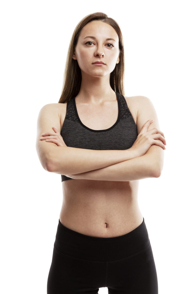 A serious slender young girl in sportswear is standing with her