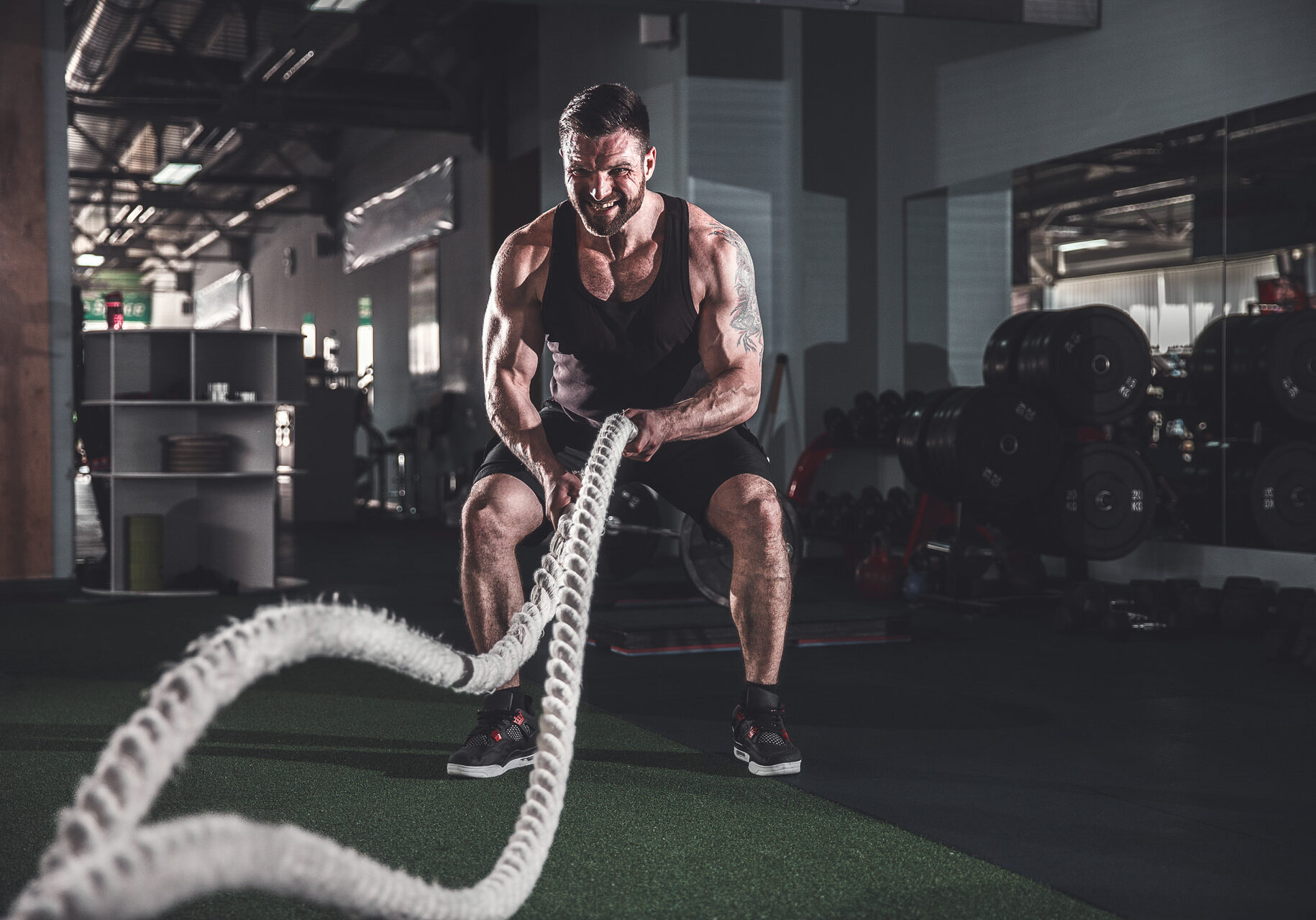 Muscular powerful aggressive man training with rope in functional training fitness gym