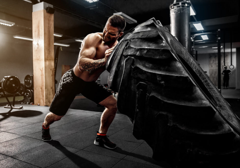 Shirtless man flipping heavy tire at crossfit gym