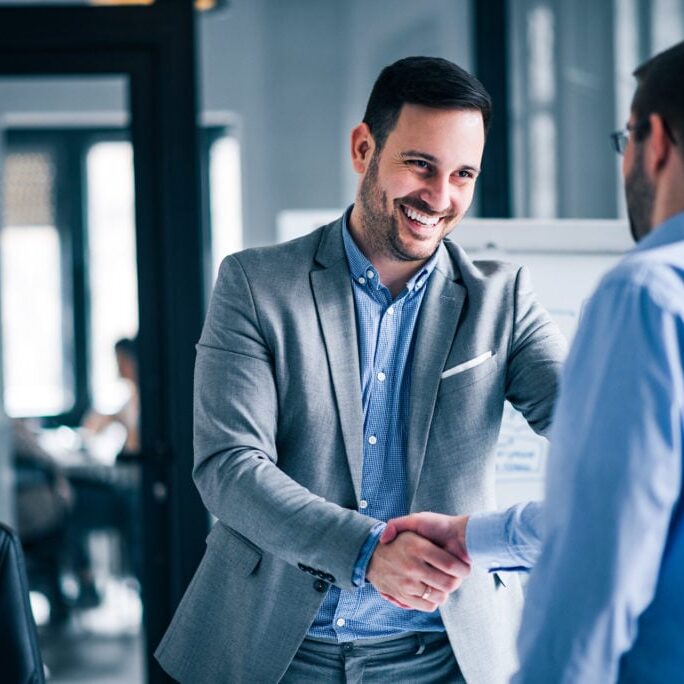 Two smiling businessmen shaking hands while standing in an offic Two smiling businessmen shaking hands while standing in an office.